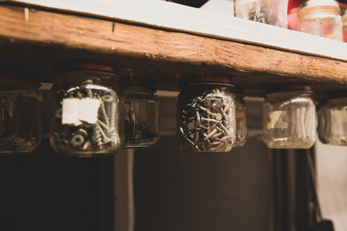 nails and screws are stored in mason jars hanging from a wooden shelf