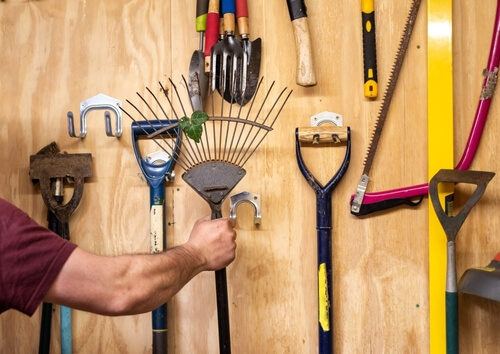 man hangs tools on the wall of a shed