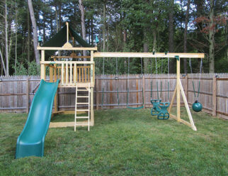 wooden swing set with green accessories sitting in a backyard